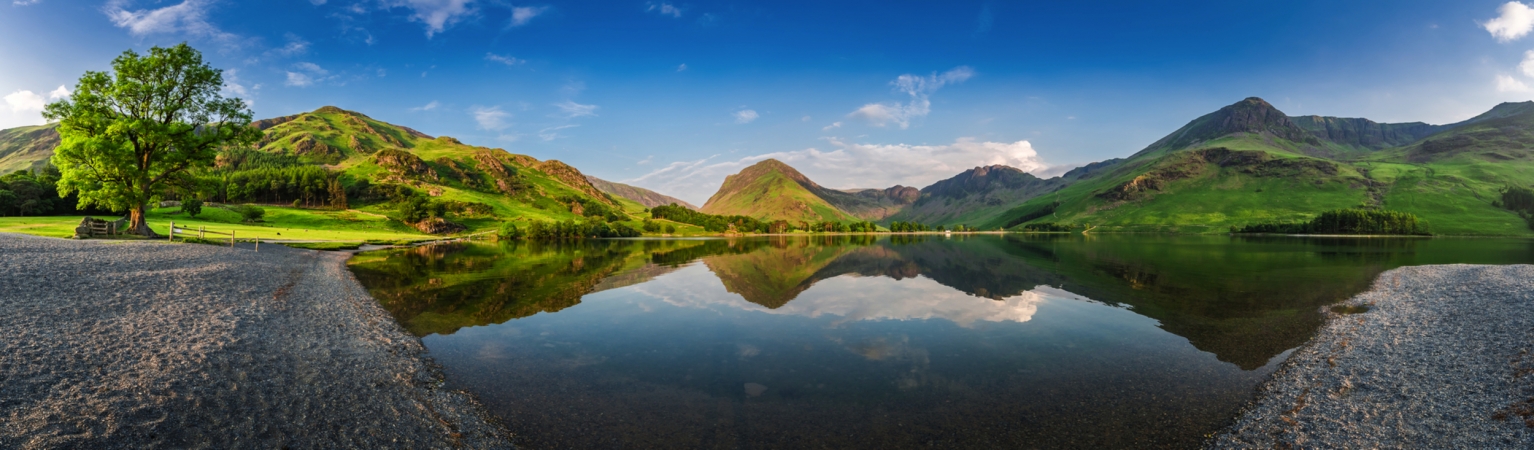 Bergsee-Landschaft mit Bäumen, grünem Hügel und blauem Himmel im Panoramaformat.