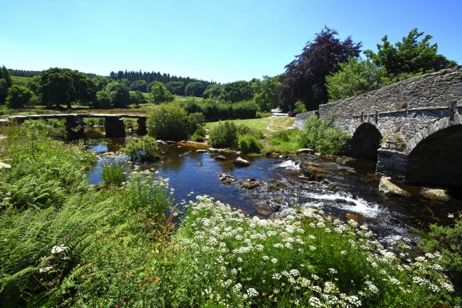 Steinbrücke über einen kleinen Fluss in einer grünen Landschaft.