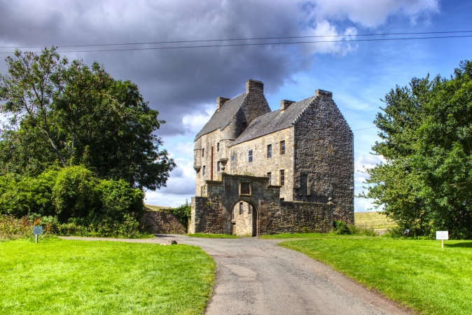Ein altes Steinschloss auf einem grünen Hügel unter bewölktem Himmel.