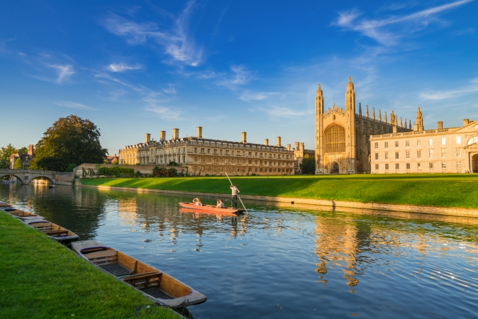 Fluss mit Booten vor der Universitätsgebäude der University of Cambridge bei sonnigem Wetter.