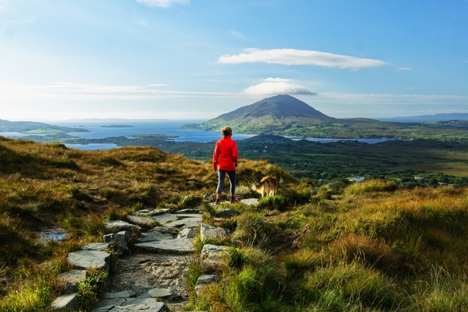 Frau wandert im Connemara-Nationalpark in Irland mit Blick auf die Berge und das Meer in der Ferne.