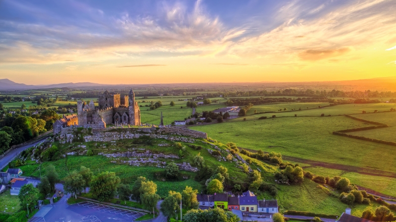 Burg auf Hügel in grüner Landschaft bei Sonnenuntergang.