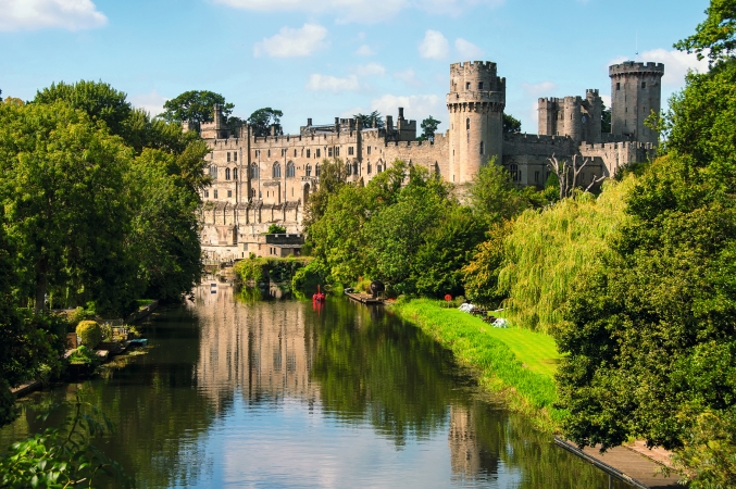 Schloss am Fluss, umgeben von Bäumen, an einem sonnigen Tag.