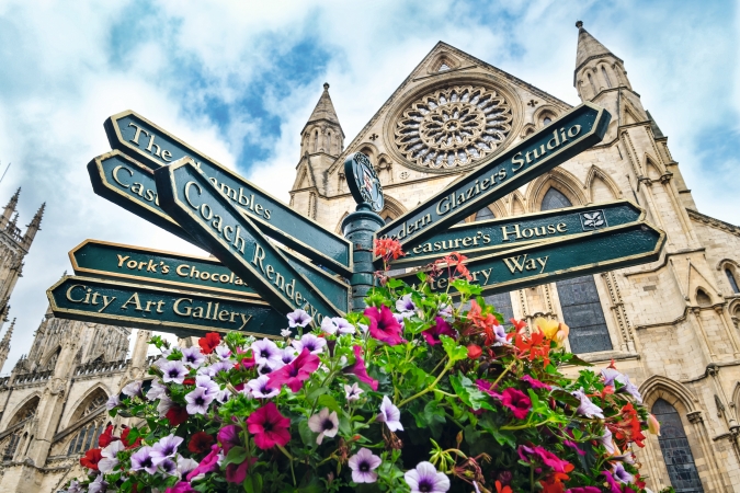 Wegweiser vor gotischer Kathedrale in York, umgeben von Blumen.