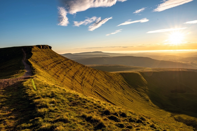 Landschaft mit Hügeln und Sonnenaufgang im Hintergrund