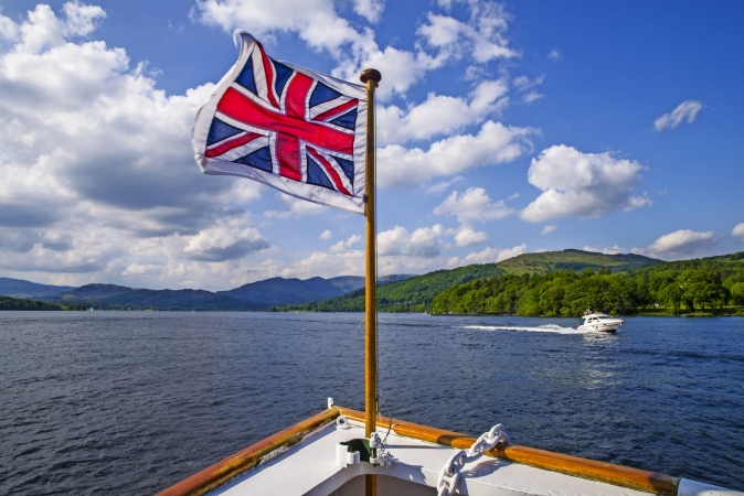 Boot mit britischer Flagge, See und Hügel im Hintergrund.