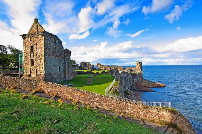 Ruine einer alten Burg an der Küste mit Meer im Hintergrund bei blauem Himmel.